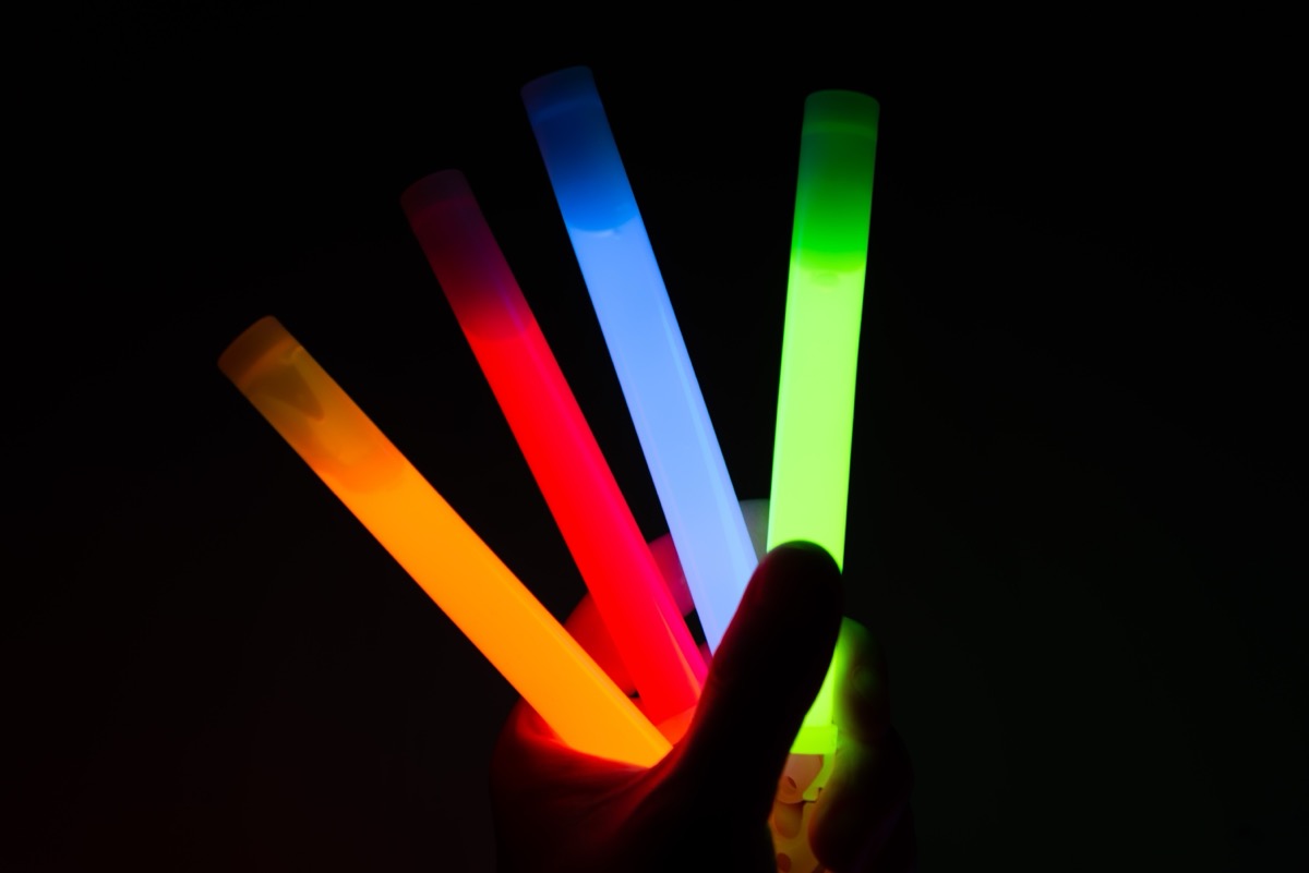 A person holds four differently colored glow sticks in the dark.