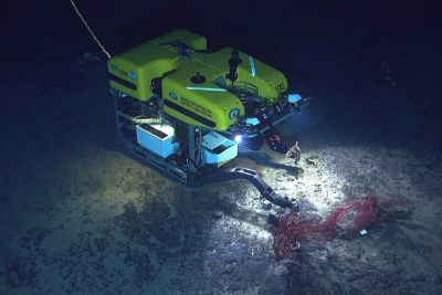 a undersea robot is using its arms to examine a red sea creature on the sea floor