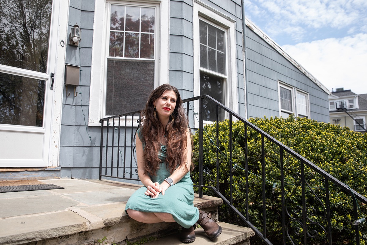 white woman sitting on steps outside of house, looking pensive