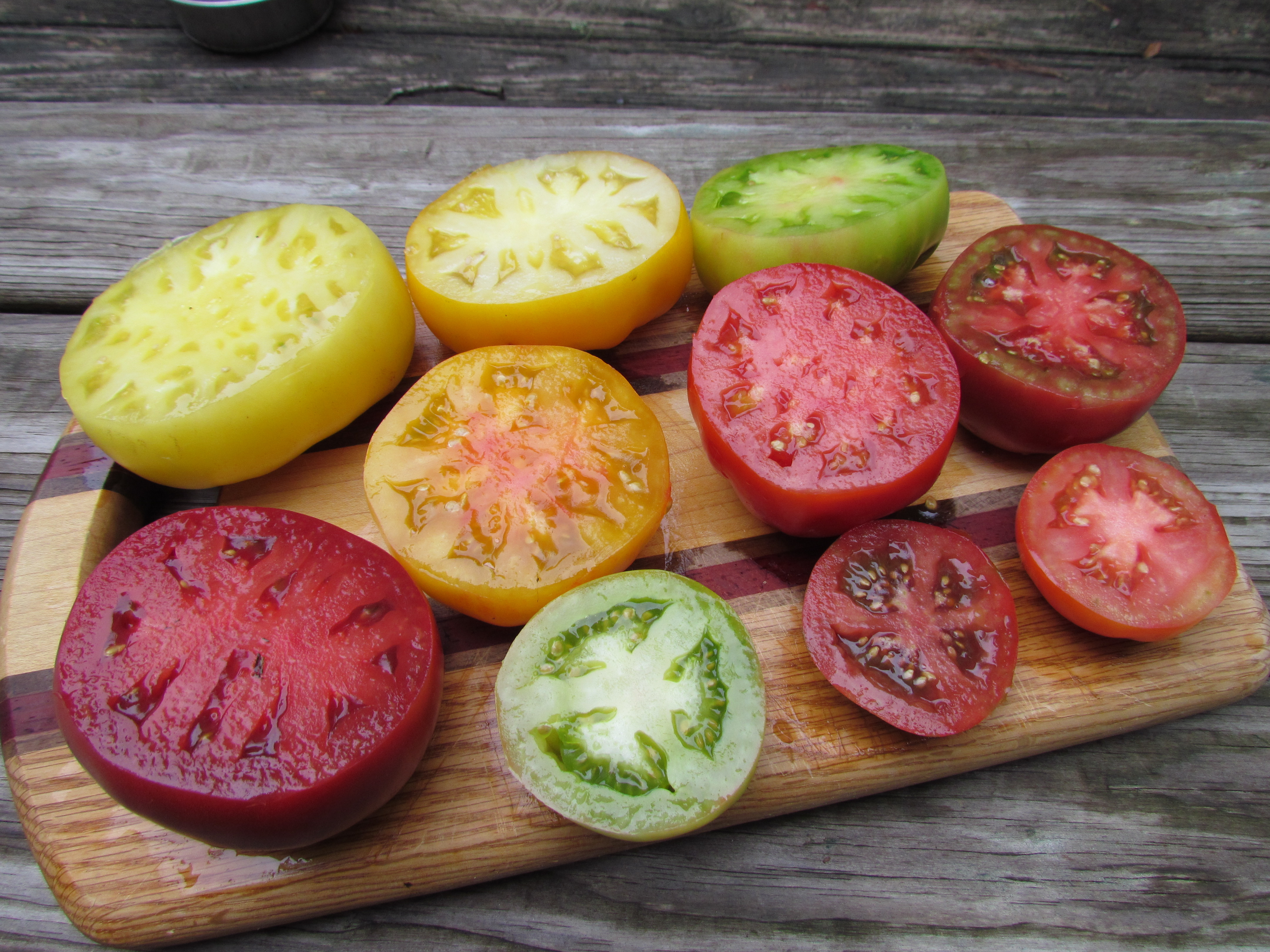 10 tomatoes sliced in half on a cutting board that are red, orange, yellow, and green.