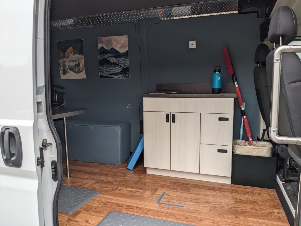 The inside of a van, outfitted with a small storage cabinet, padded floors, and a desk.
