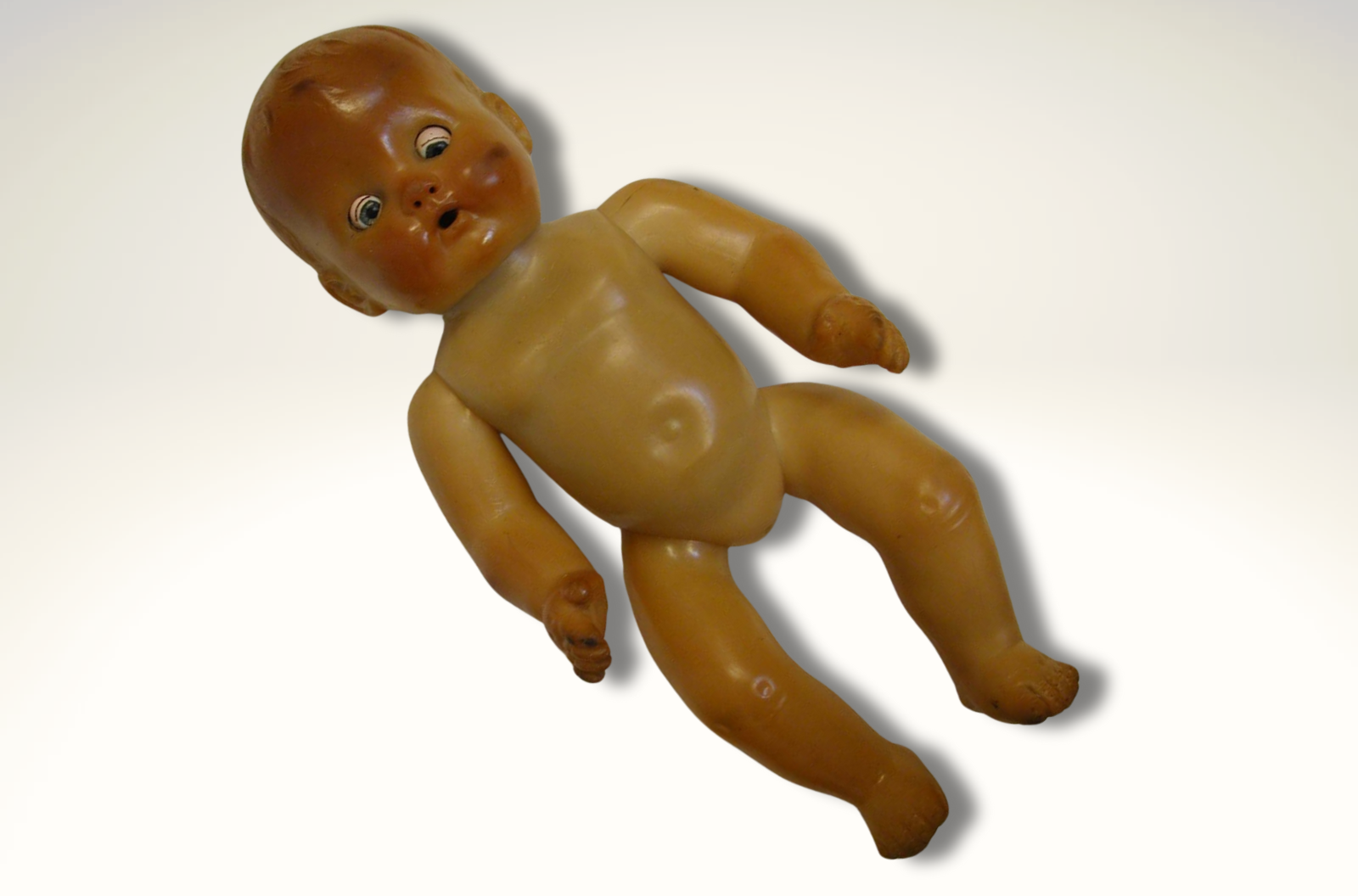 A photo of an old plastic baby doll. While most of the body is pinkish-tan, the face, hands, and legs fade into a rusty brown color.