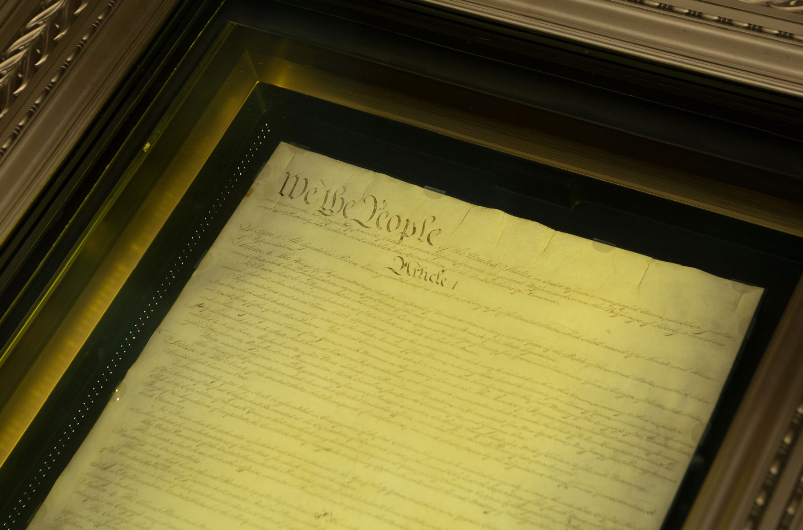 A document is housed in an ornate gold frame and covered with glass.It reads, "We the people..."