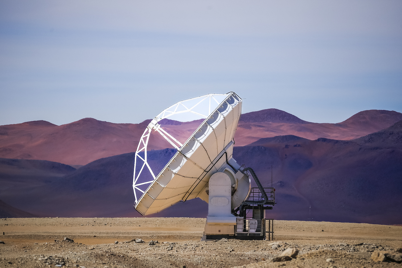 A satellite pointed up at the sky, with purple mountains in the background.