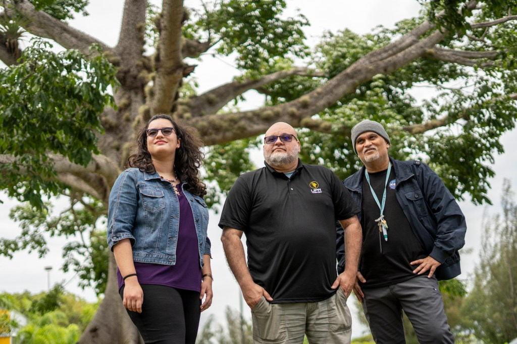 Three people standing outdoors, two men and one woman.