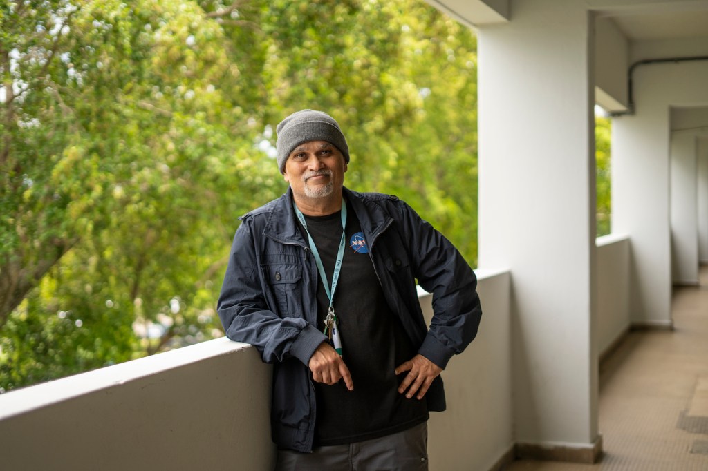 A man wearing a beanie and a NASA shirt leans on a bannister.