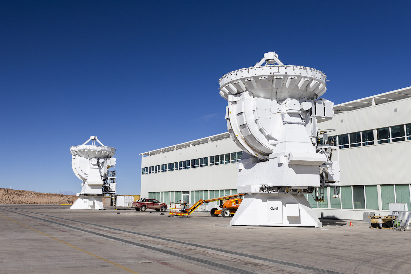 Two giant white structures sit in front of a two story white building.