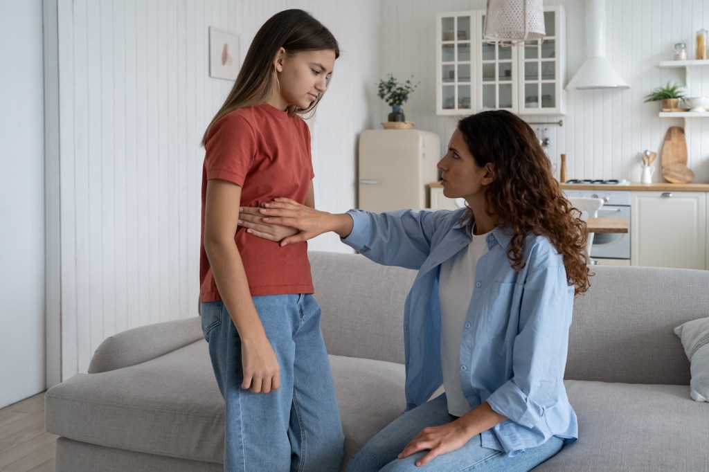 A mother feeling a preteen girl's upset stomach from period cramps