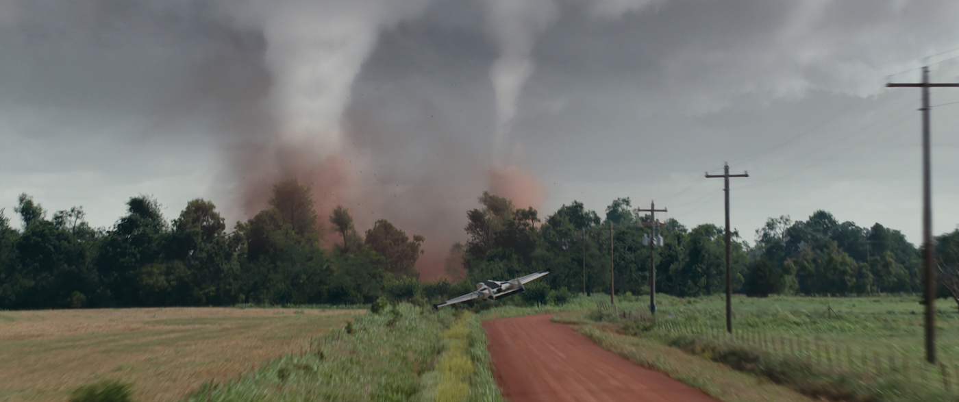 Two tornadoes, one large and one smaller, on the horizon of a pastoral landscape. A drone flies at them.