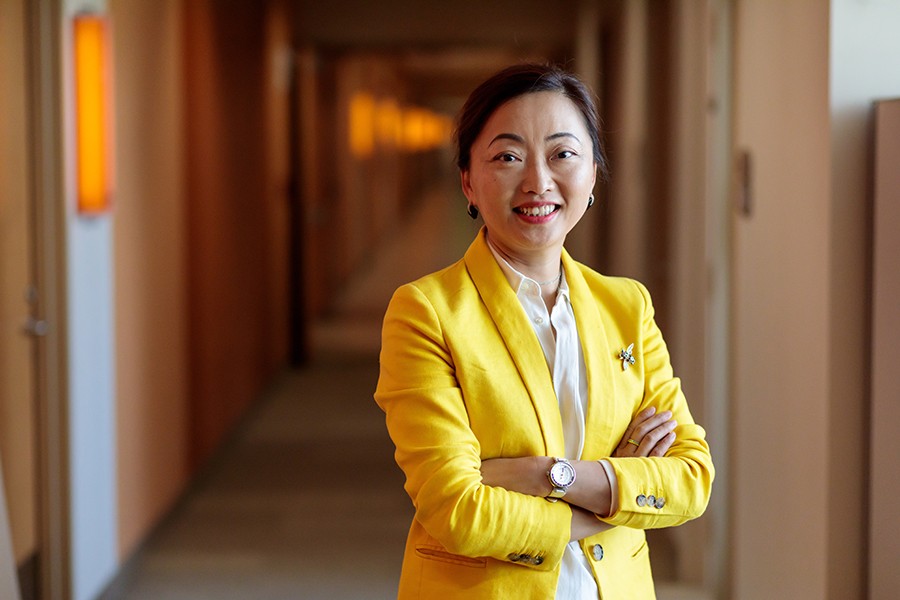A woman wearing a yellow blazer smiles in a hallway