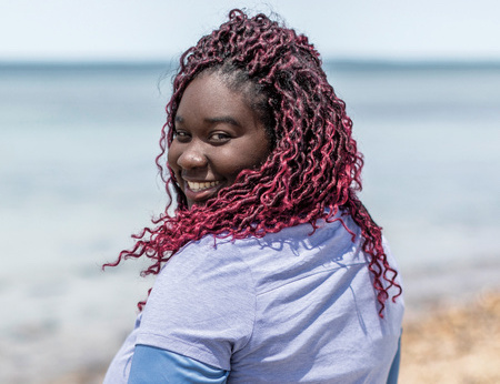 A Black woman smiles over her shoulder on the beach.