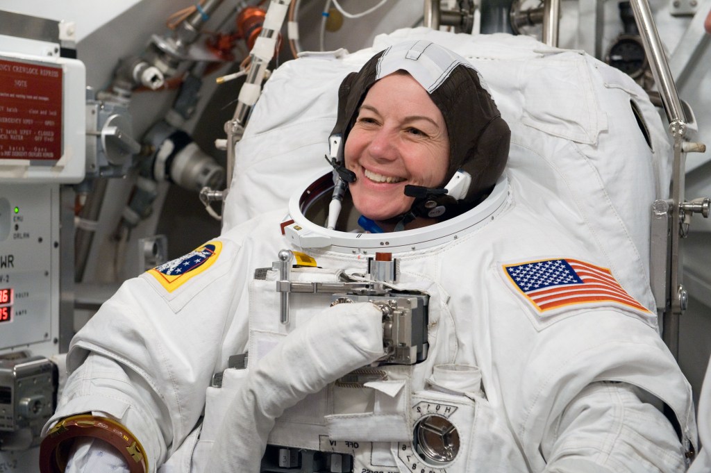 A white woman in a bulky astronaut suit with black-and-white cap, laughing