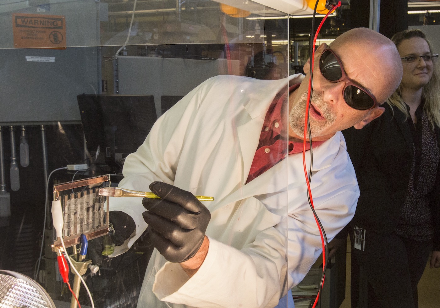 A man wearing sunglasses paints a clear fluid onto a glass panel