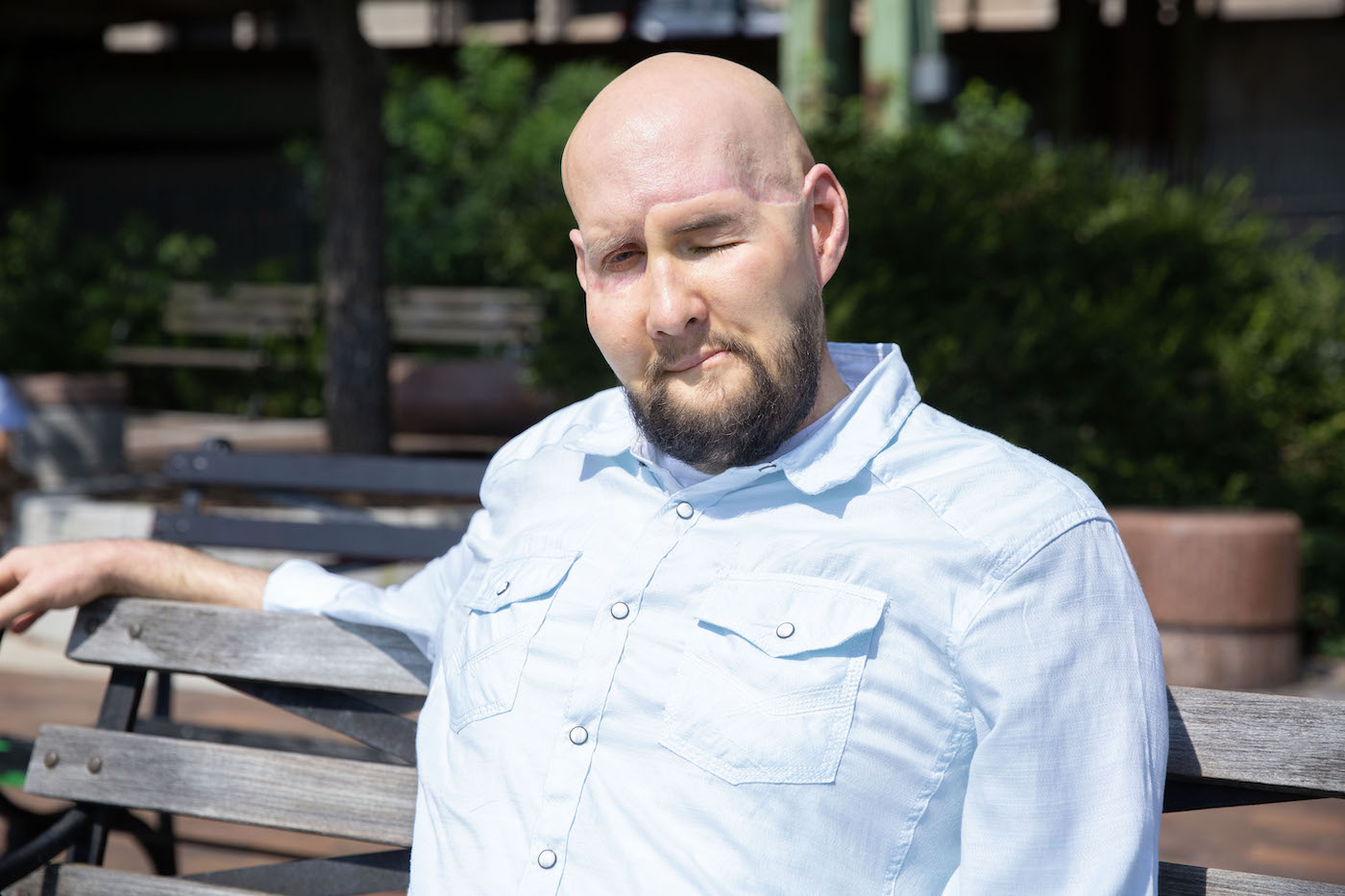 A man sitting on a bench, with one eye closed.