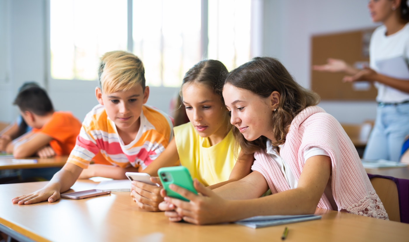 Group of kids using smartphones during lesson in school. Girls and boys using gadgets while studying.