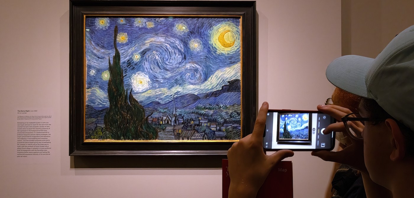 A person taking a photo of The Starry Night using their smartphone.