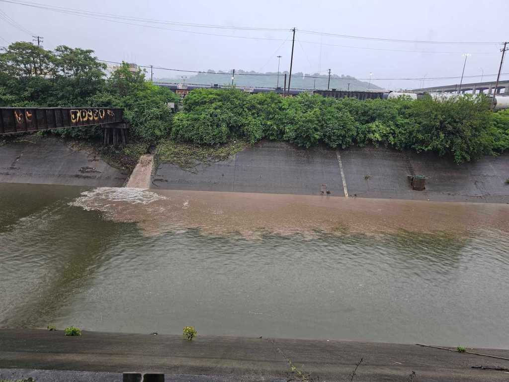 Sewage pouring into a body of water running through a town, discoloring the water.