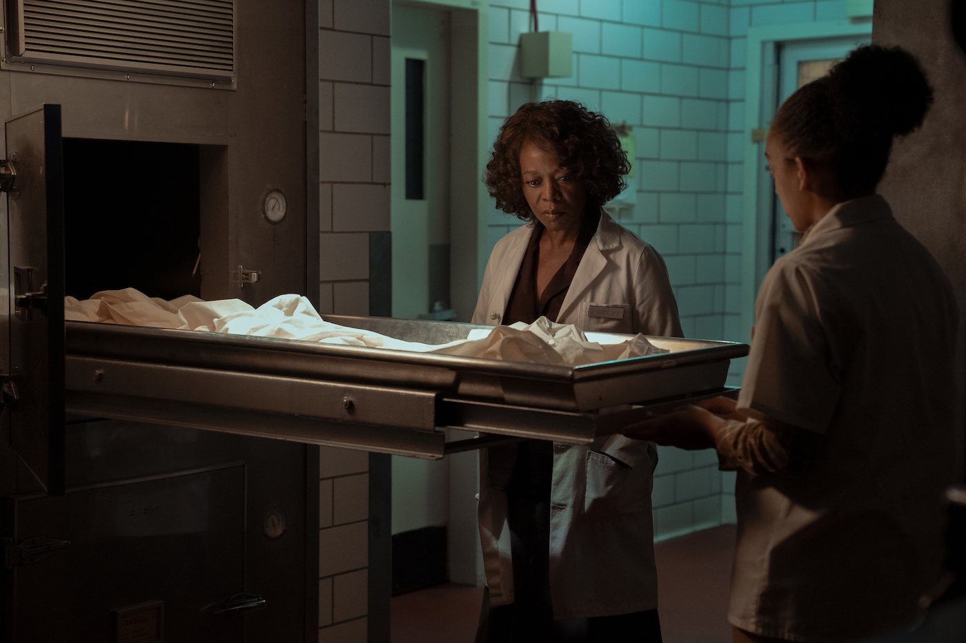 a woman looks at a mortuary drawer, where a body should be. it's empty.