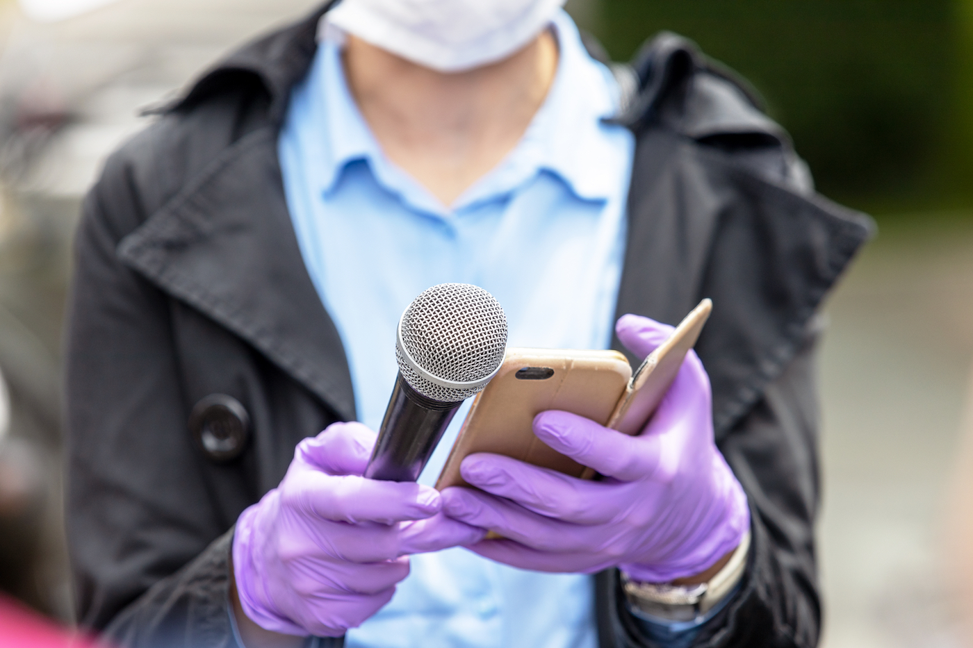 Journalist wearing protective gloves and face mask against coronavirus COVID-19 disease holding microphone making media interview during virus pandemic