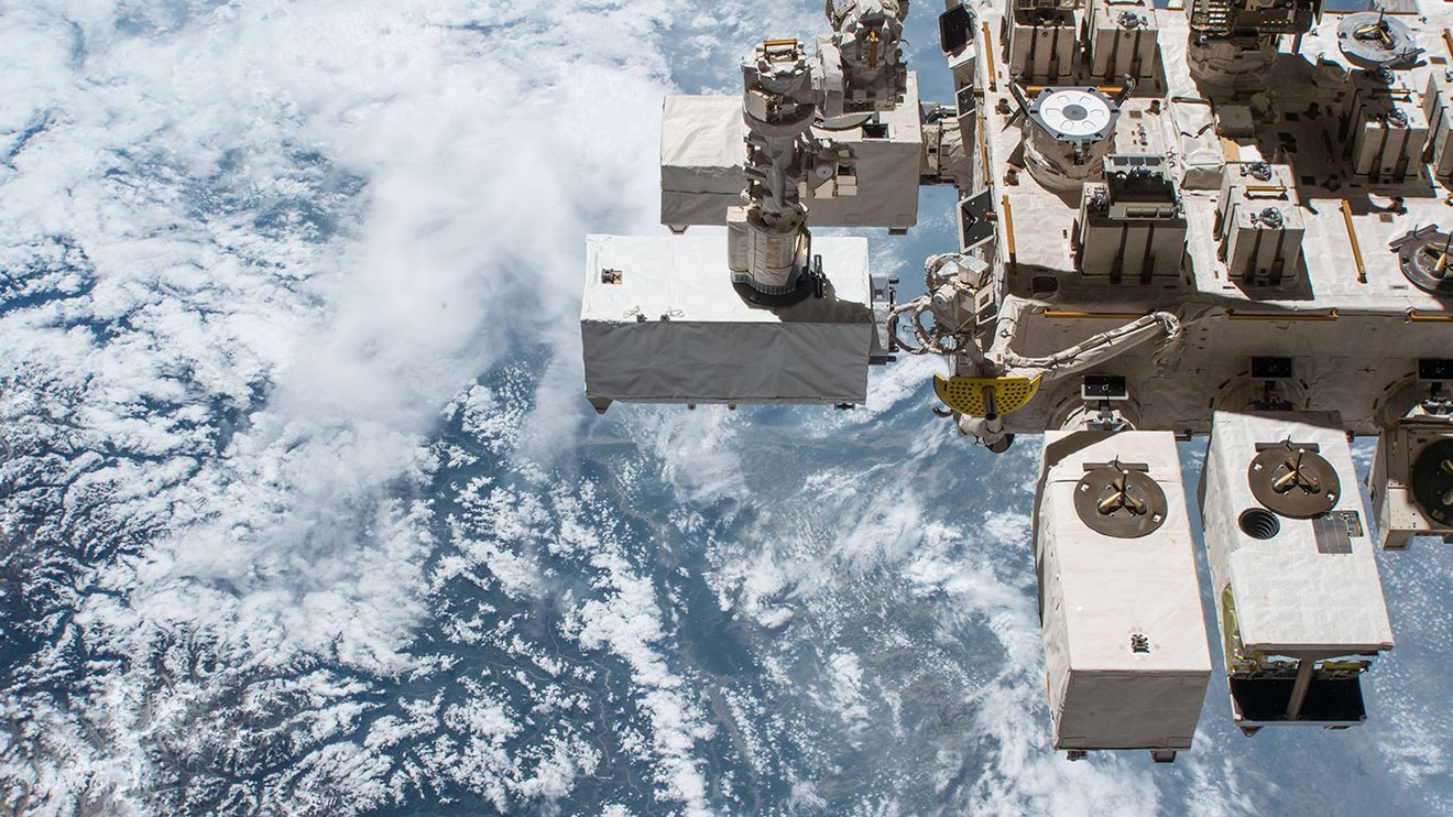 A sensor module encased in big blocky white metal cases attached to the International Space Station floating high above the Earth.