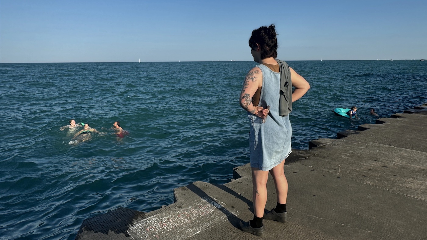 A person stands on a dock watching friends swim around in Lake Michigan.