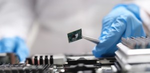 Fingers in blue gloves are holding a microchip with tweezers, close-up, blurry. Professional repair of electronic equipment