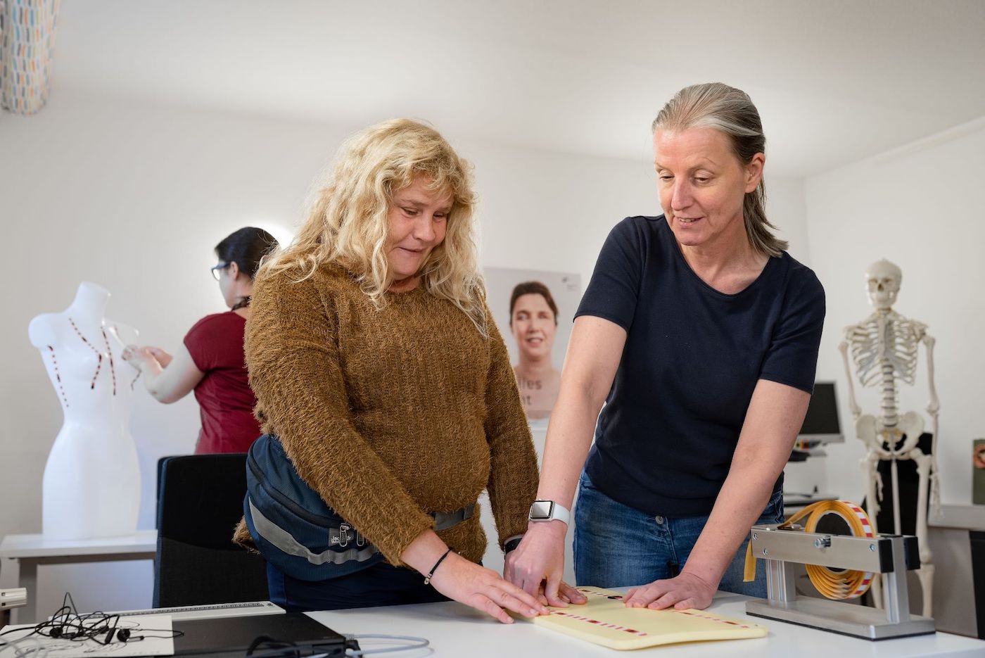 Two women touch a pad with texture on it in a medical room.