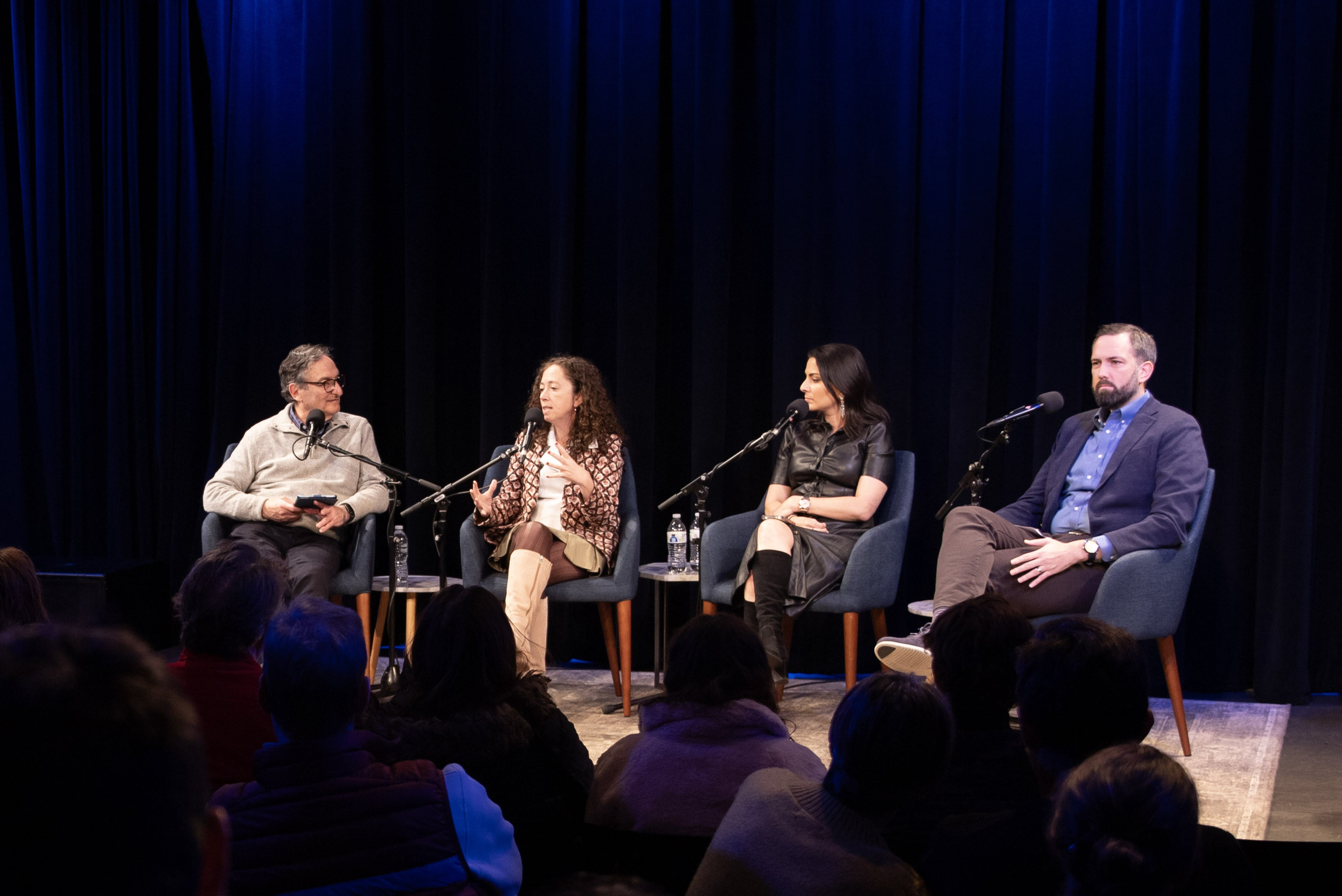 Four people sitting on stage having a conversation into microphones