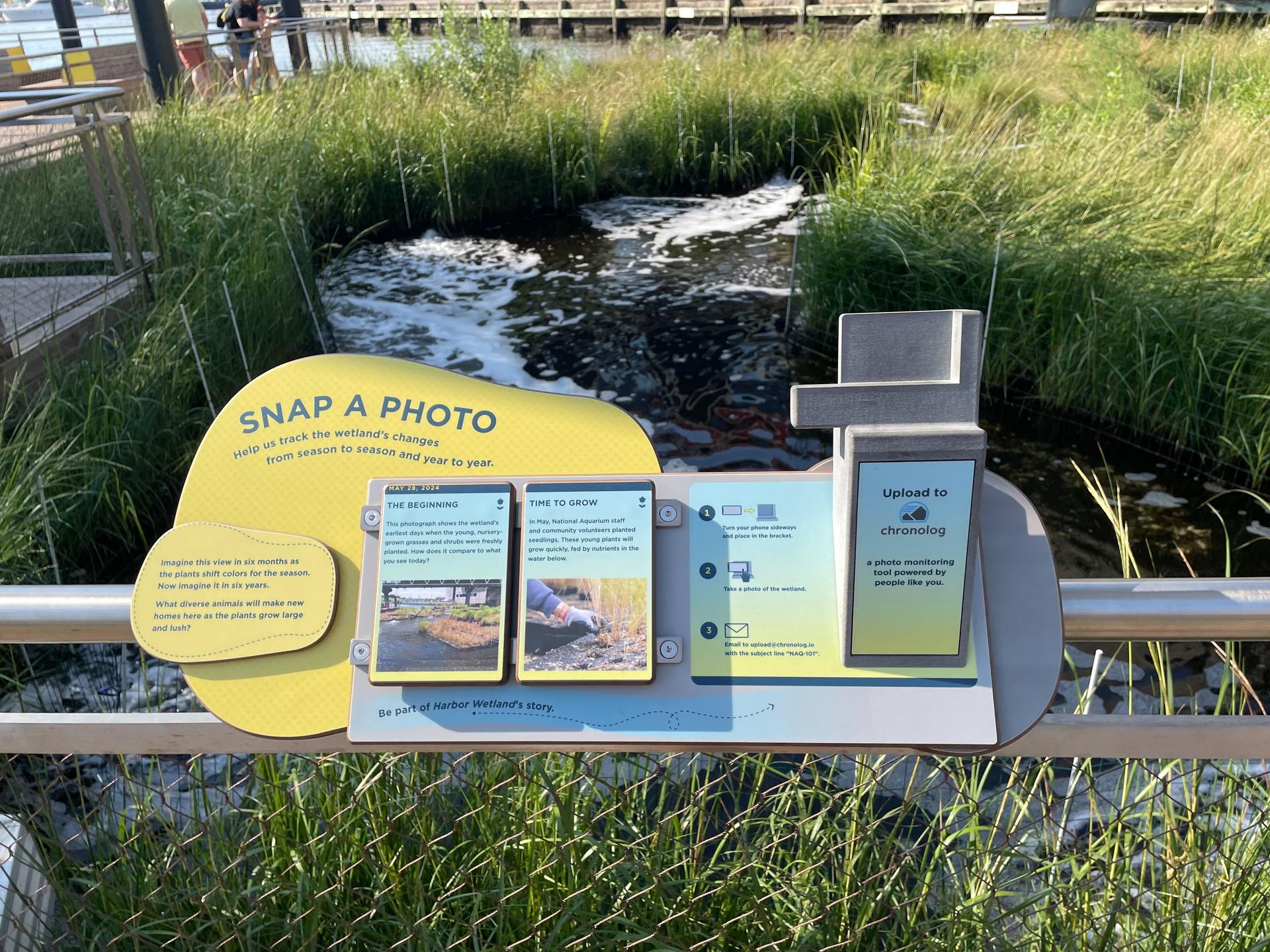 A sign that says "snap a photo" in front of a marsh area.