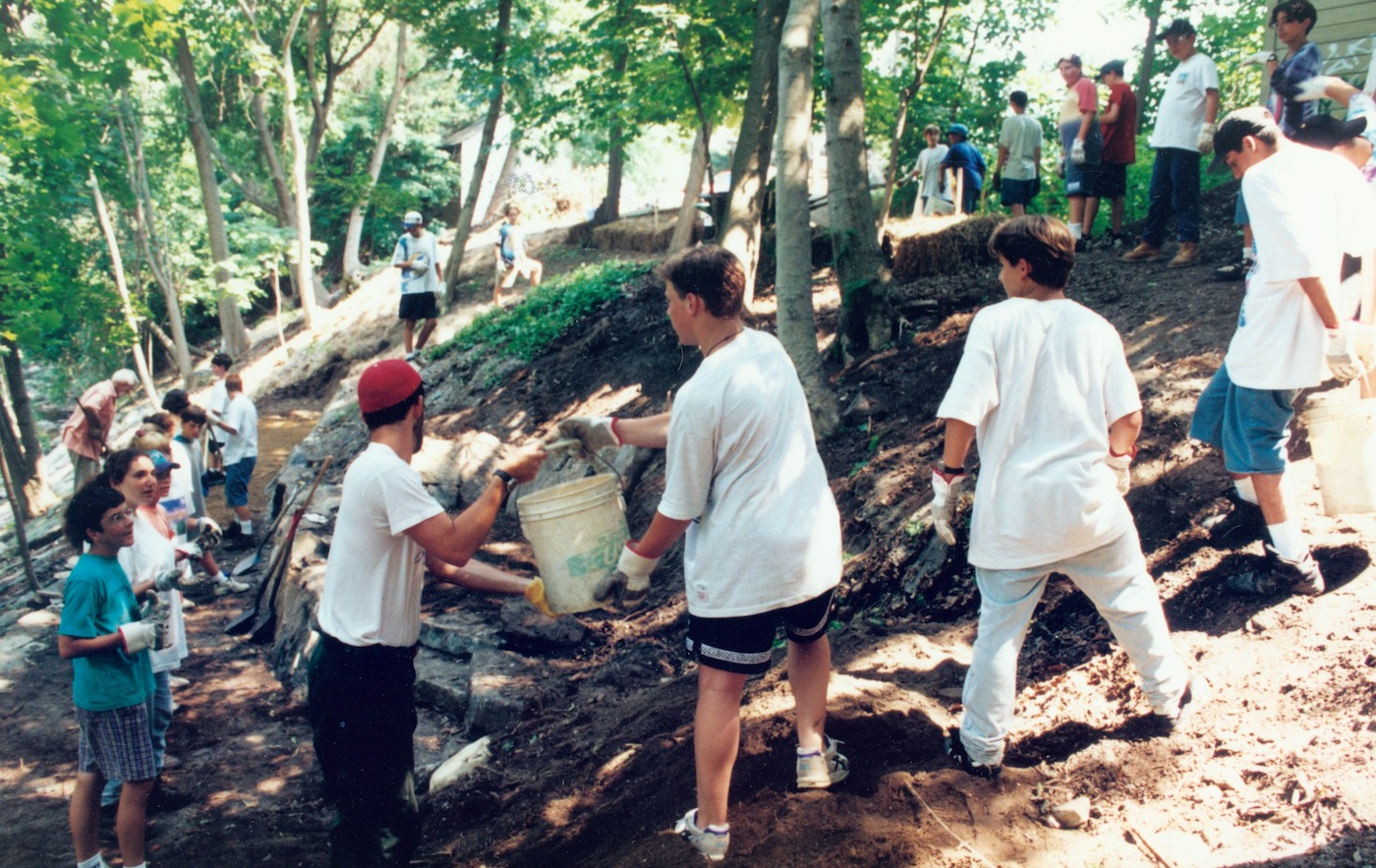 A line of people passing buckets on a nature trail.