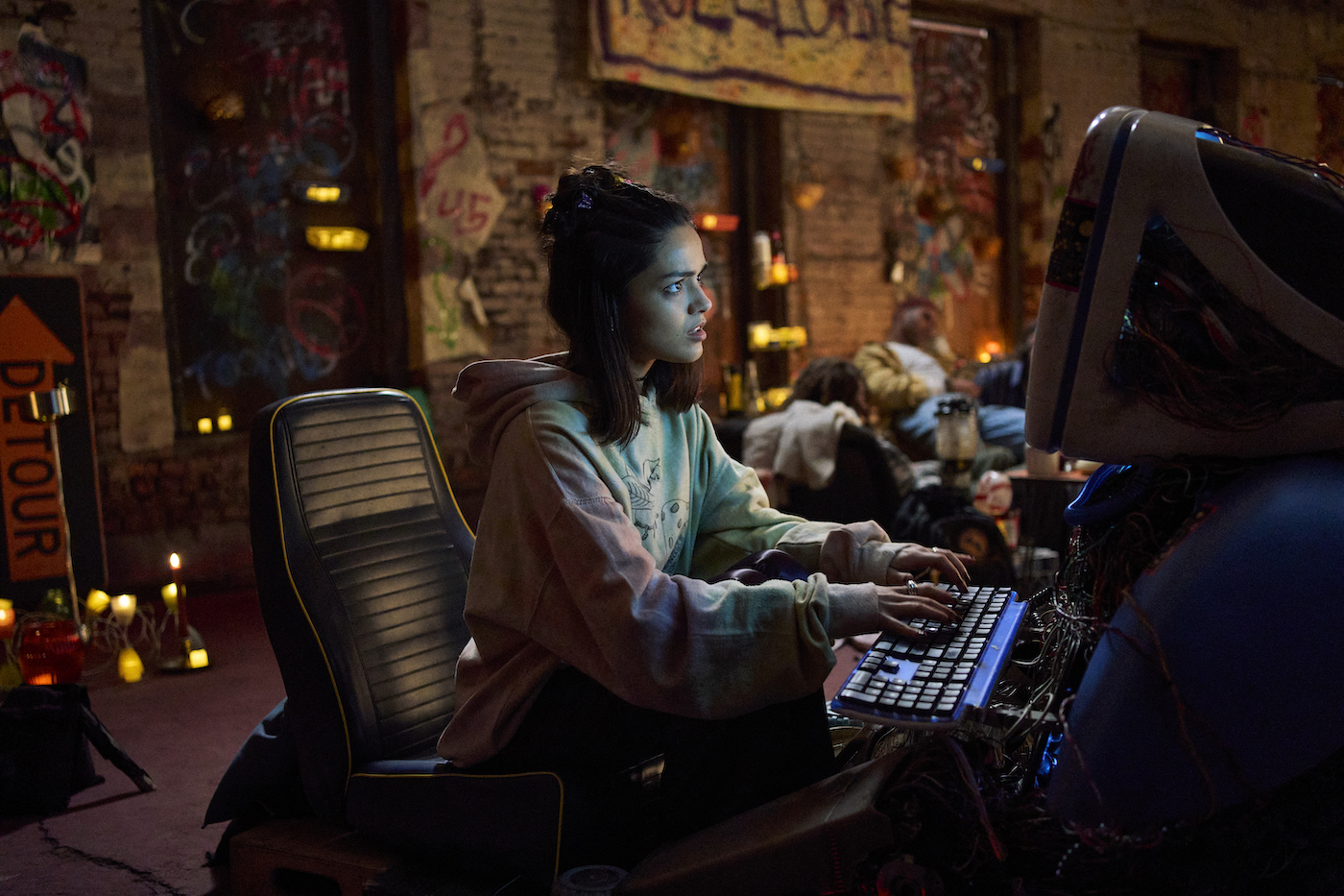 A young woman typing at a computer in a disorganized house.