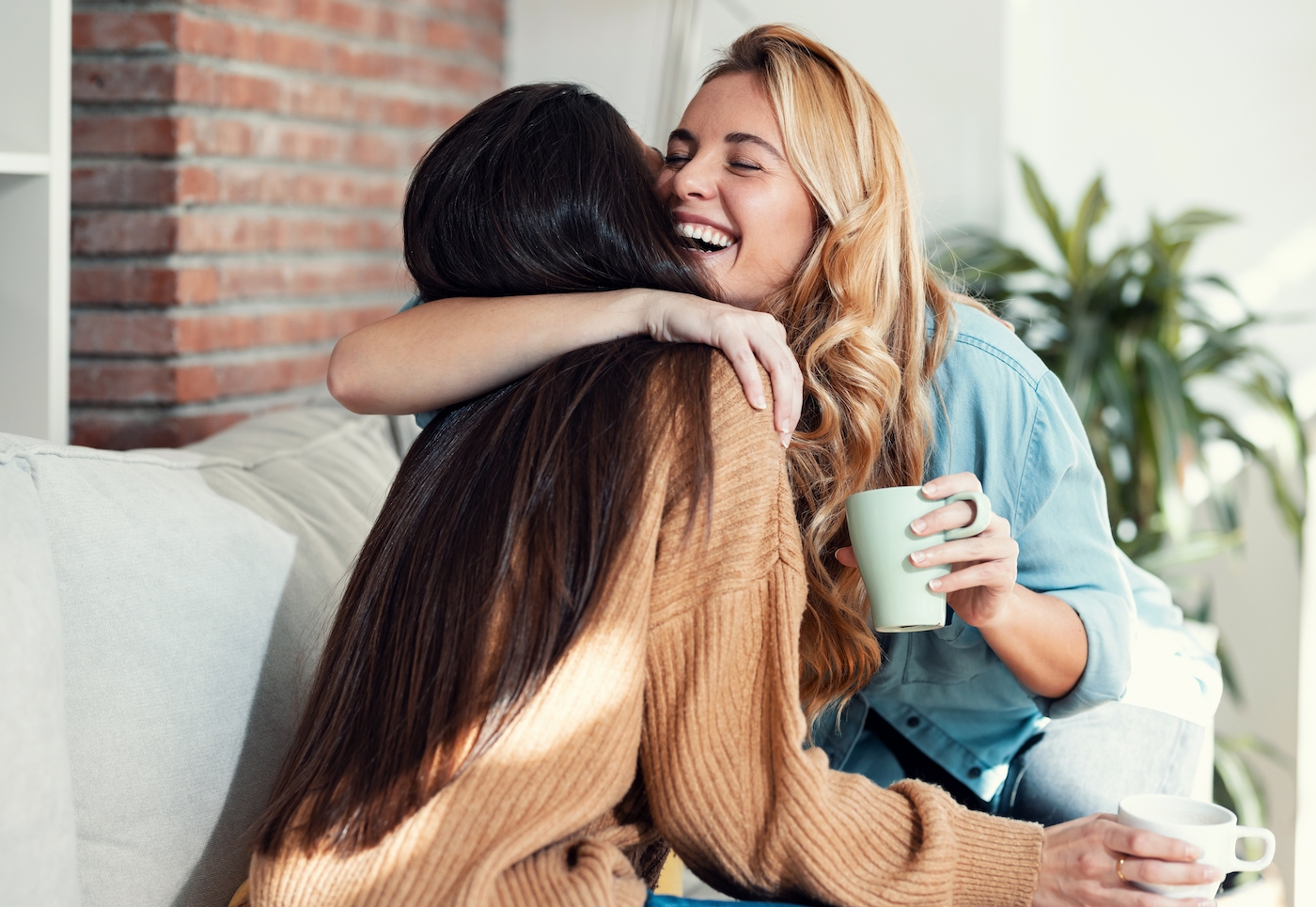 Shot of two lovely smiling women hugging each other while talking sitting on couch in the living room at home.