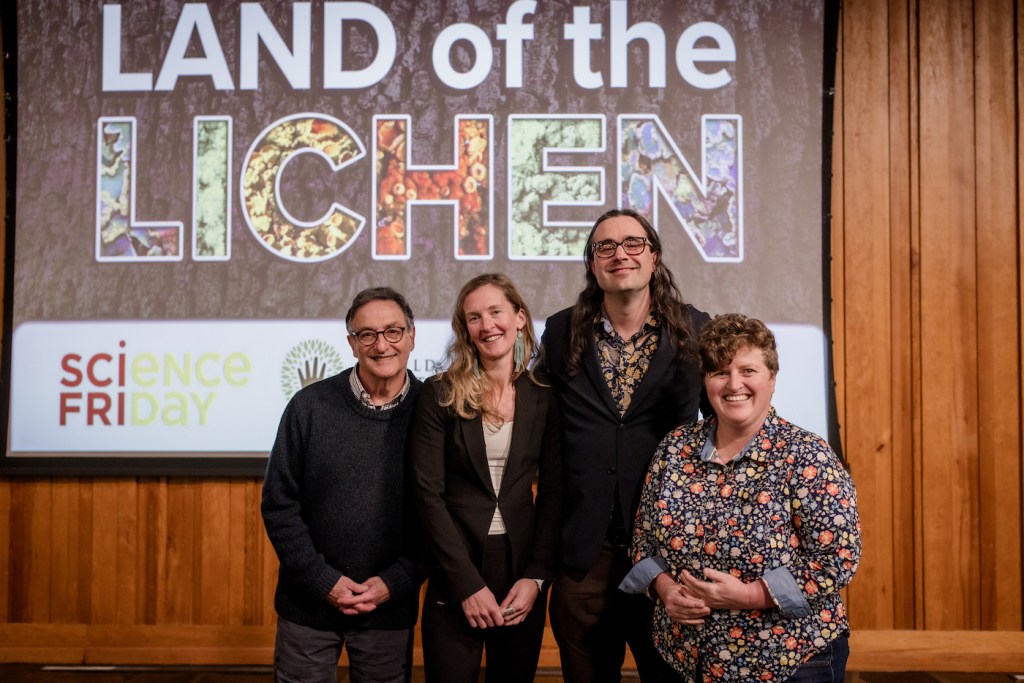 Four people stand in front of a sign that says "Land of the Lichen"