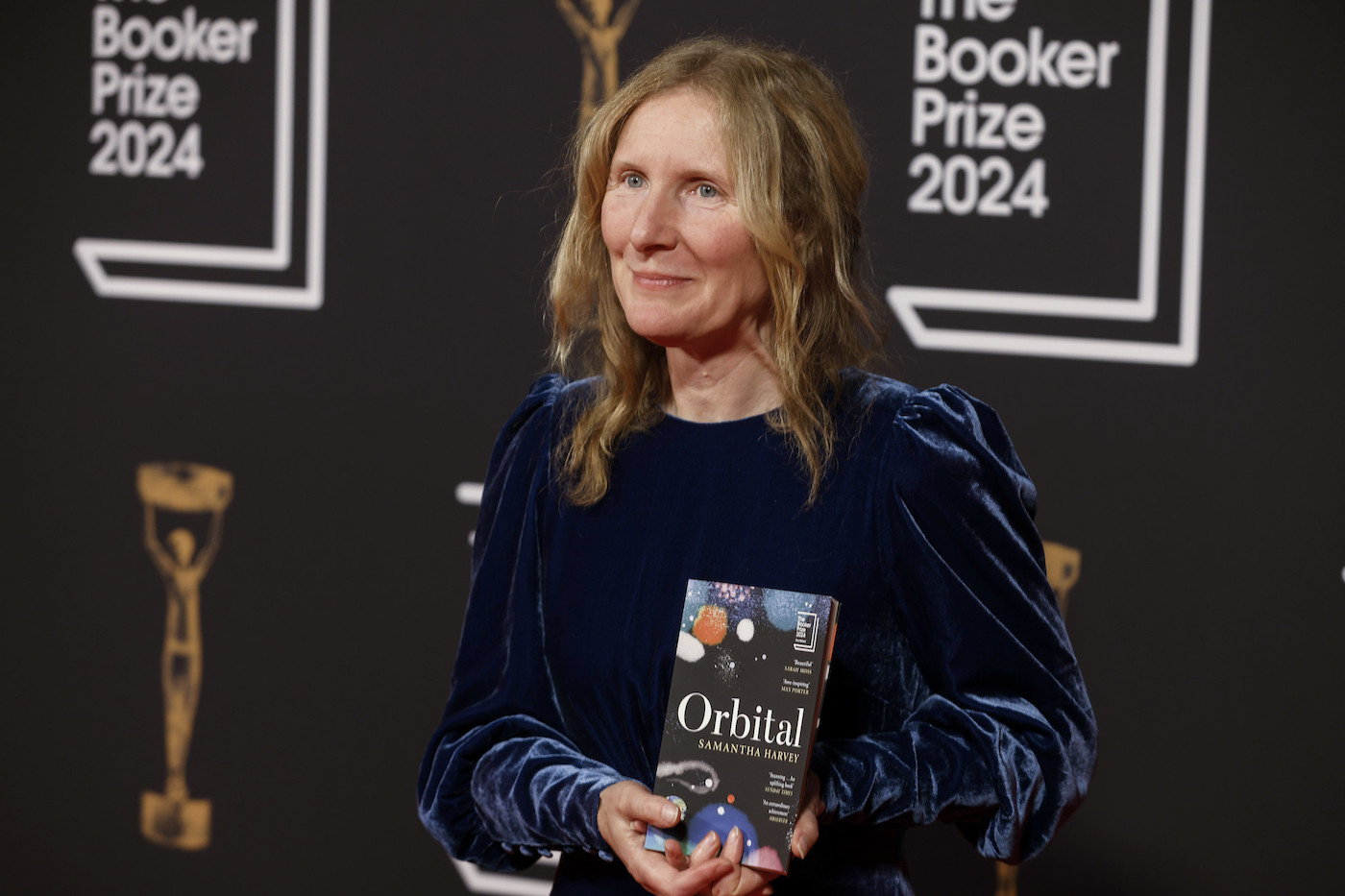 A woman holds the book "Orbital" in front of a background that says "The Booker Prize 2024"