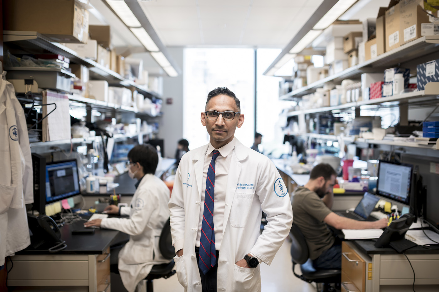 A man wearing glasses and a lab coat in a biology lab.