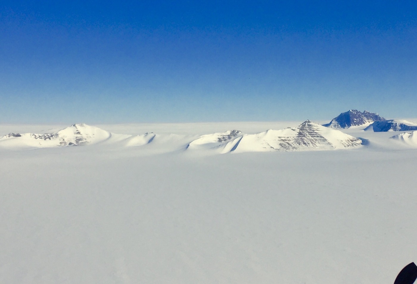 A view of a snow-covered landscape, with tops of mountains peeking out above fog.