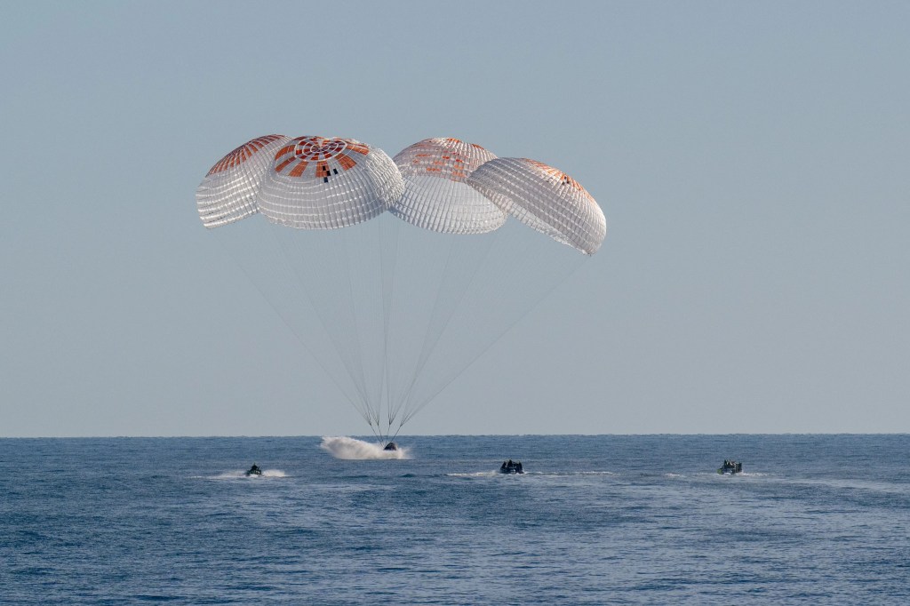 Four parachutes are deploys as a capsule lands in the ocean